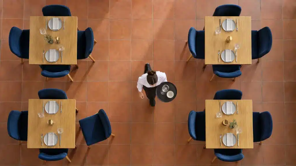 Illustration d’une salle vue du dessus avec quatre tables, une chaise reculée et une allée centrale dégagée.